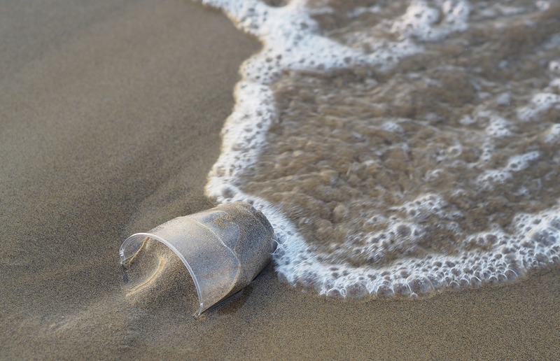 Einwegplastikbecher im Sand, der von einer Welle umspült wird