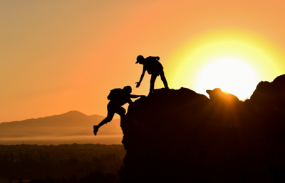 eine Person klettert einen Berg hoch, oben streckt eine andere Person ihre Hand entgegen, um zu helfen